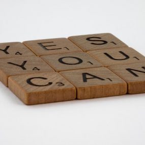 Wooden Scrabble tiles spelling 'Yes You Can' on a white background.